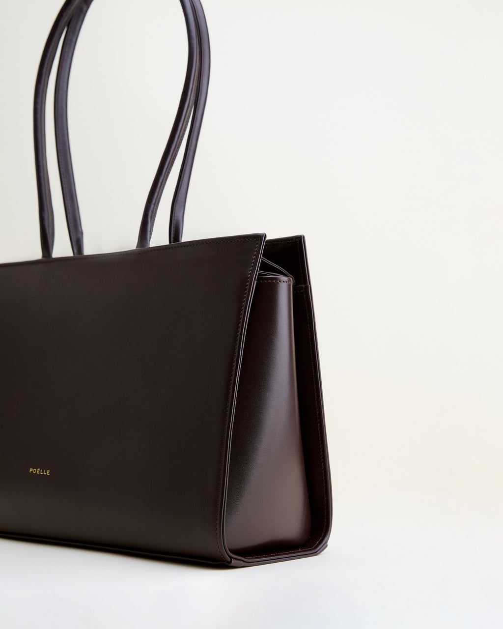 Poelle Atelier brown leather tote bag with structured design and double handles on white background