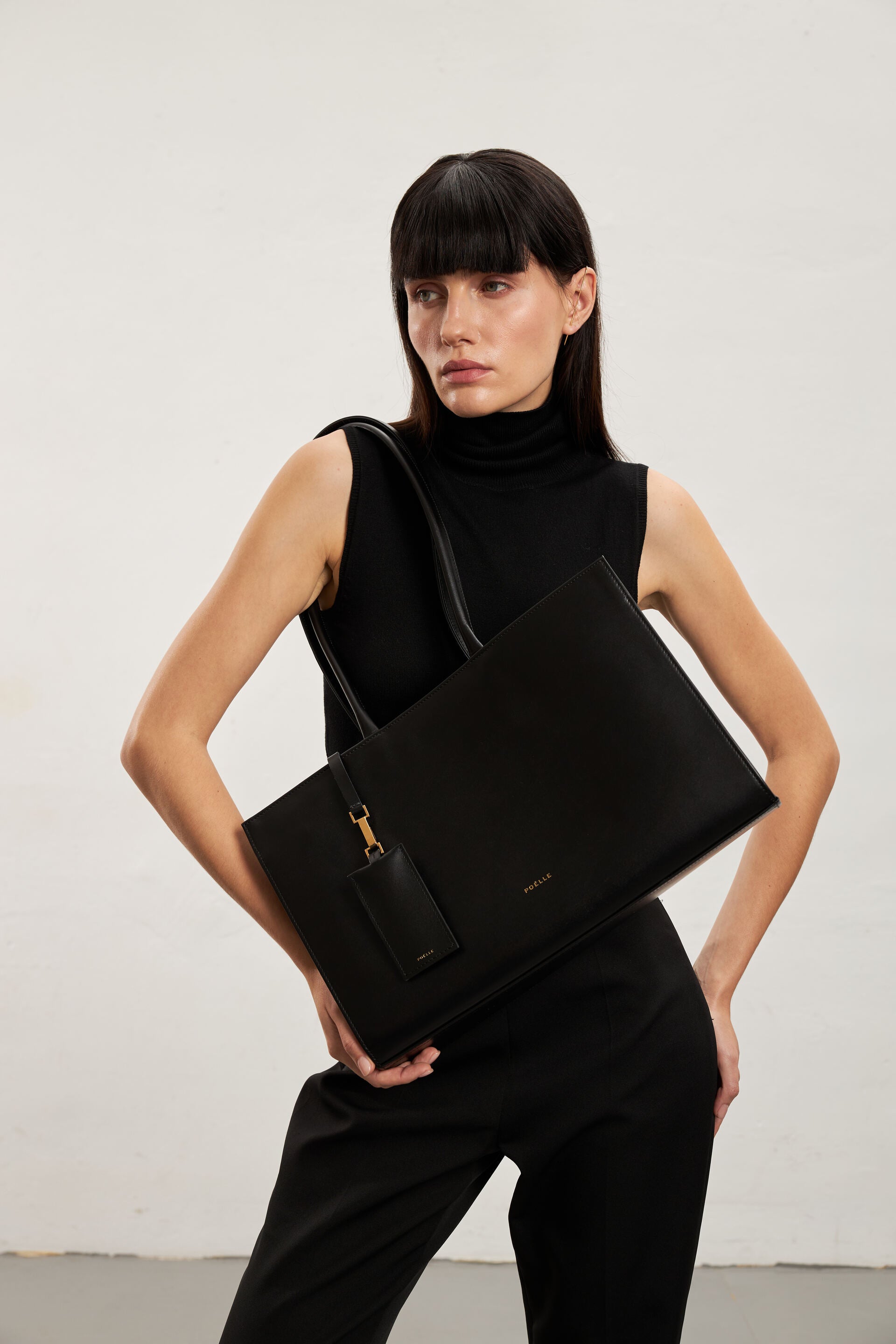 Model holding a luxury black tote bag by Poelle Atelier with sleek design and gold detail